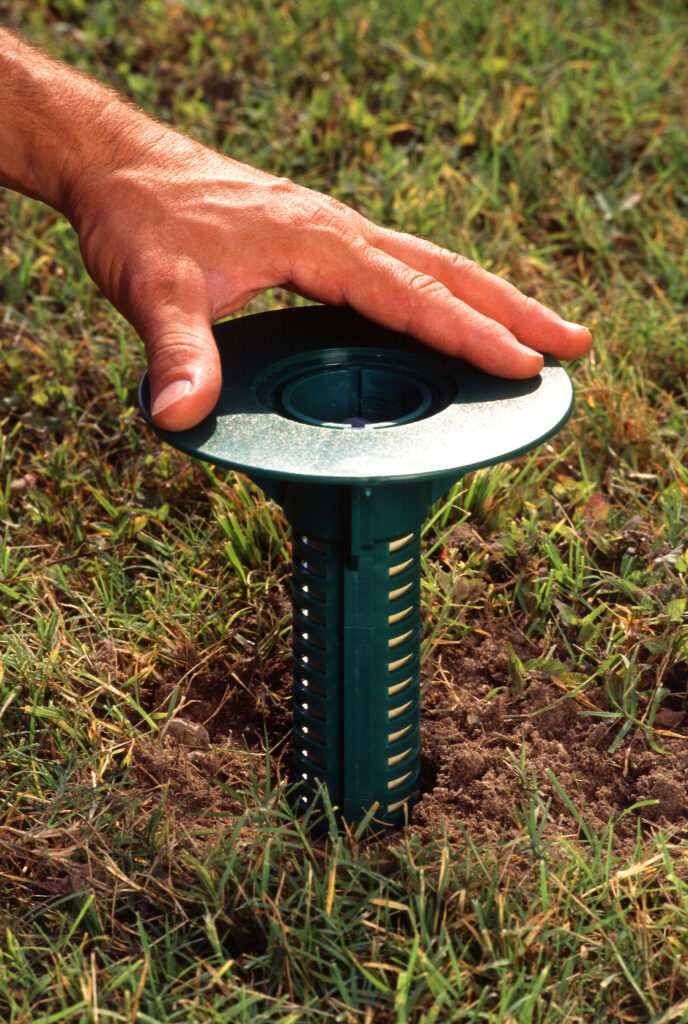 A researcher installs an in-ground termite monitoring and bait station in grass.